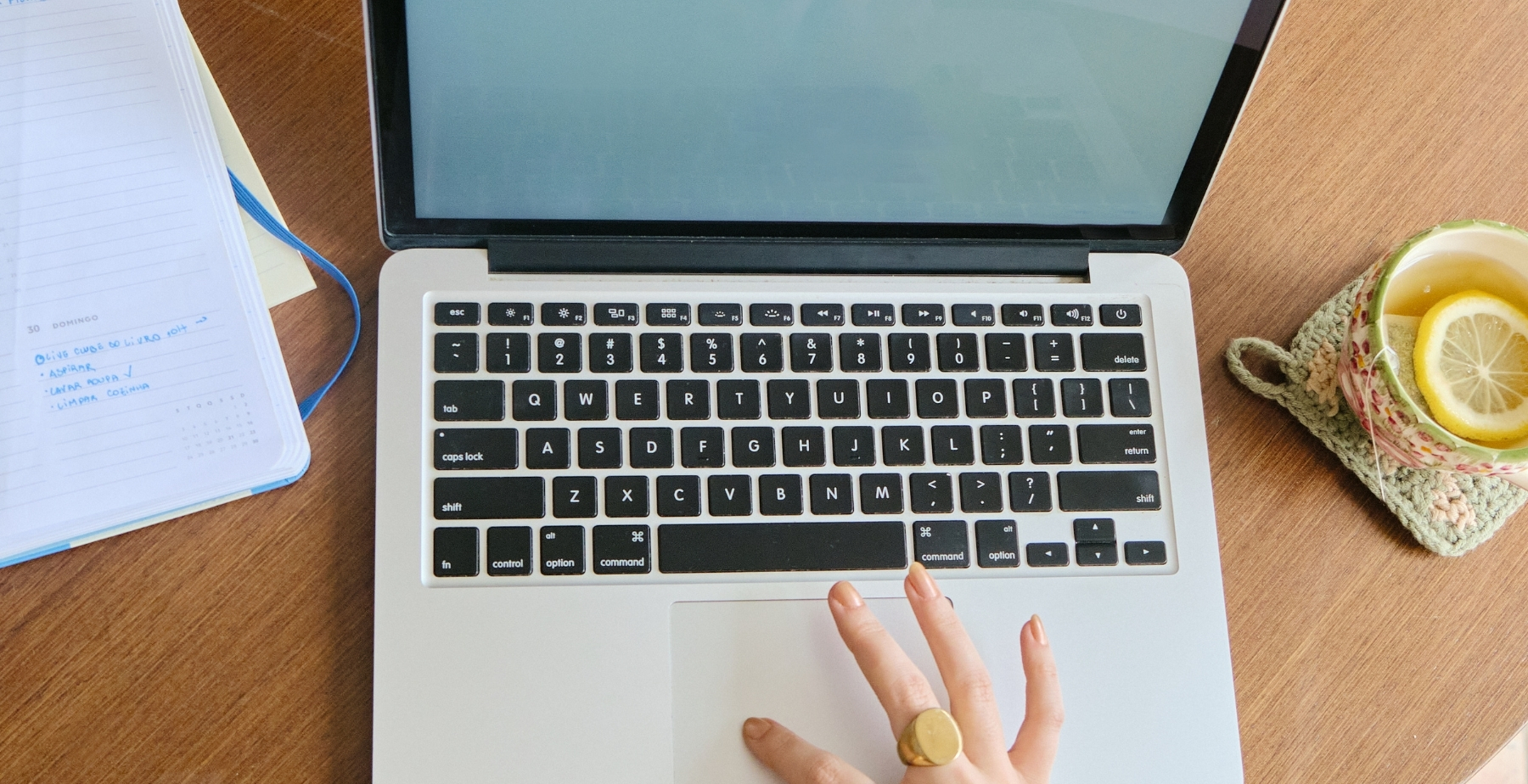 Laptop with a hand on the trackpad, surrounded by a planner and a cup of tea, illustrating productivity and digital marketing strategy development.