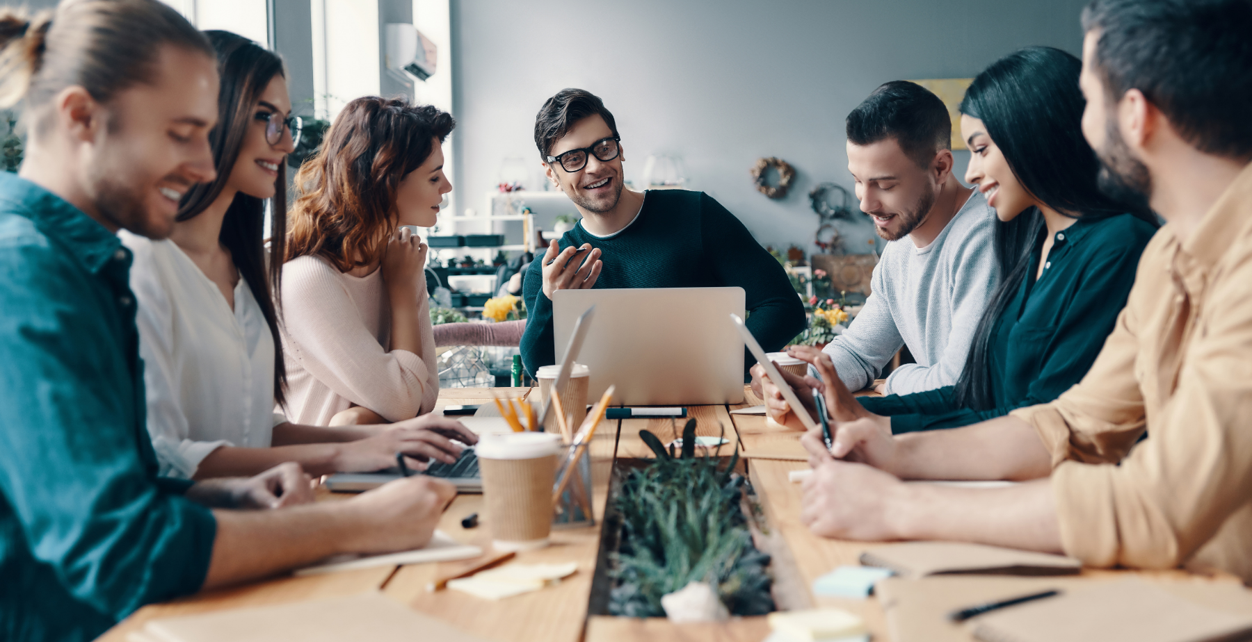 Group of diverse professionals collaborating at a table with laptops and notebooks, discussing digital marketing strategies in a modern workspace.